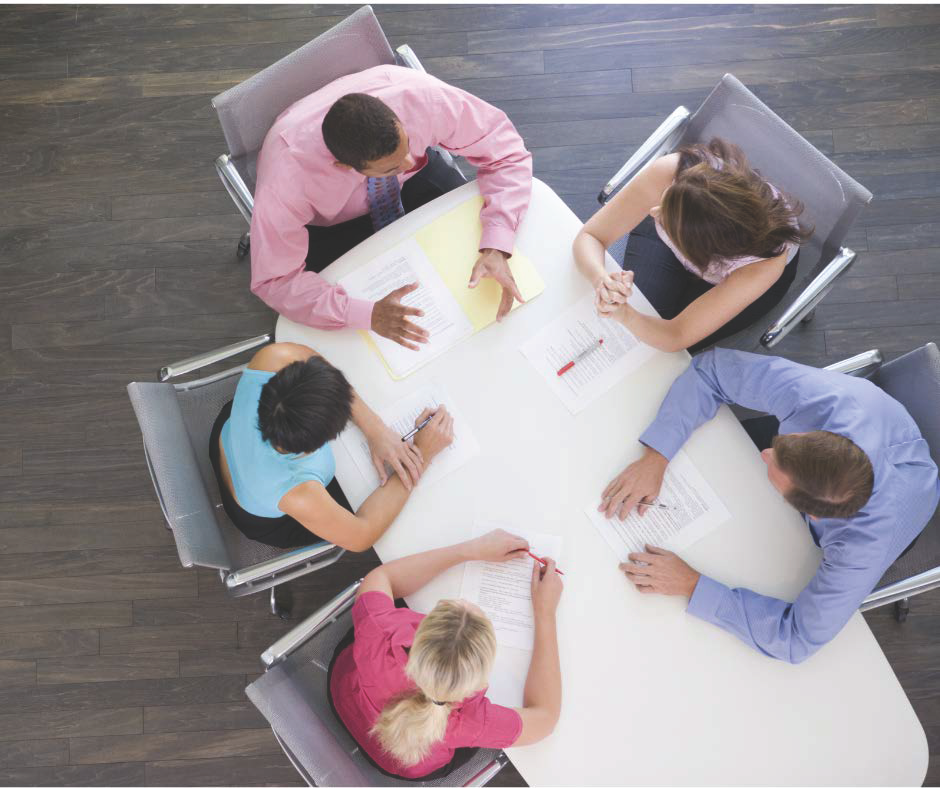 overhead shot of five people, men and women, sitting around a board table