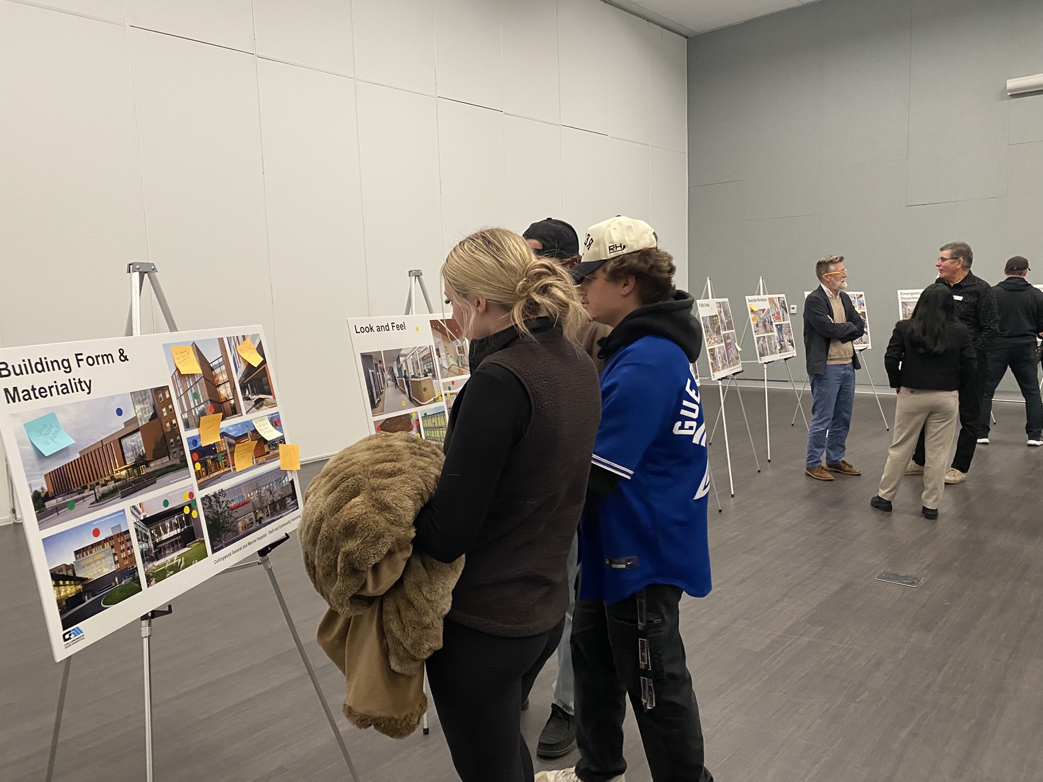 A young female and two males stand by a poster board of new hospital design concepts.