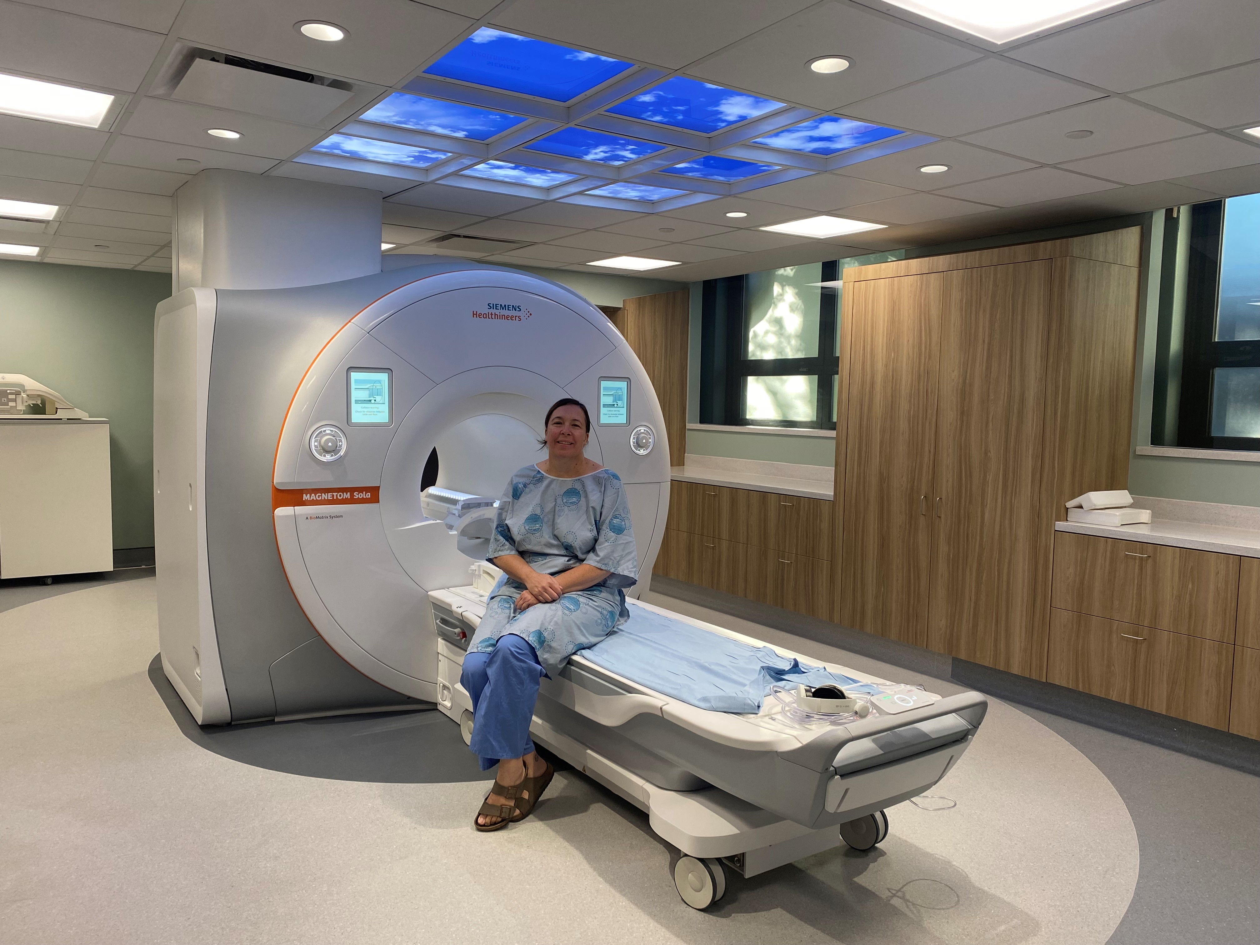 woman wearing blue hosptial gown sits of the bed of the hospitals new MRI suite.