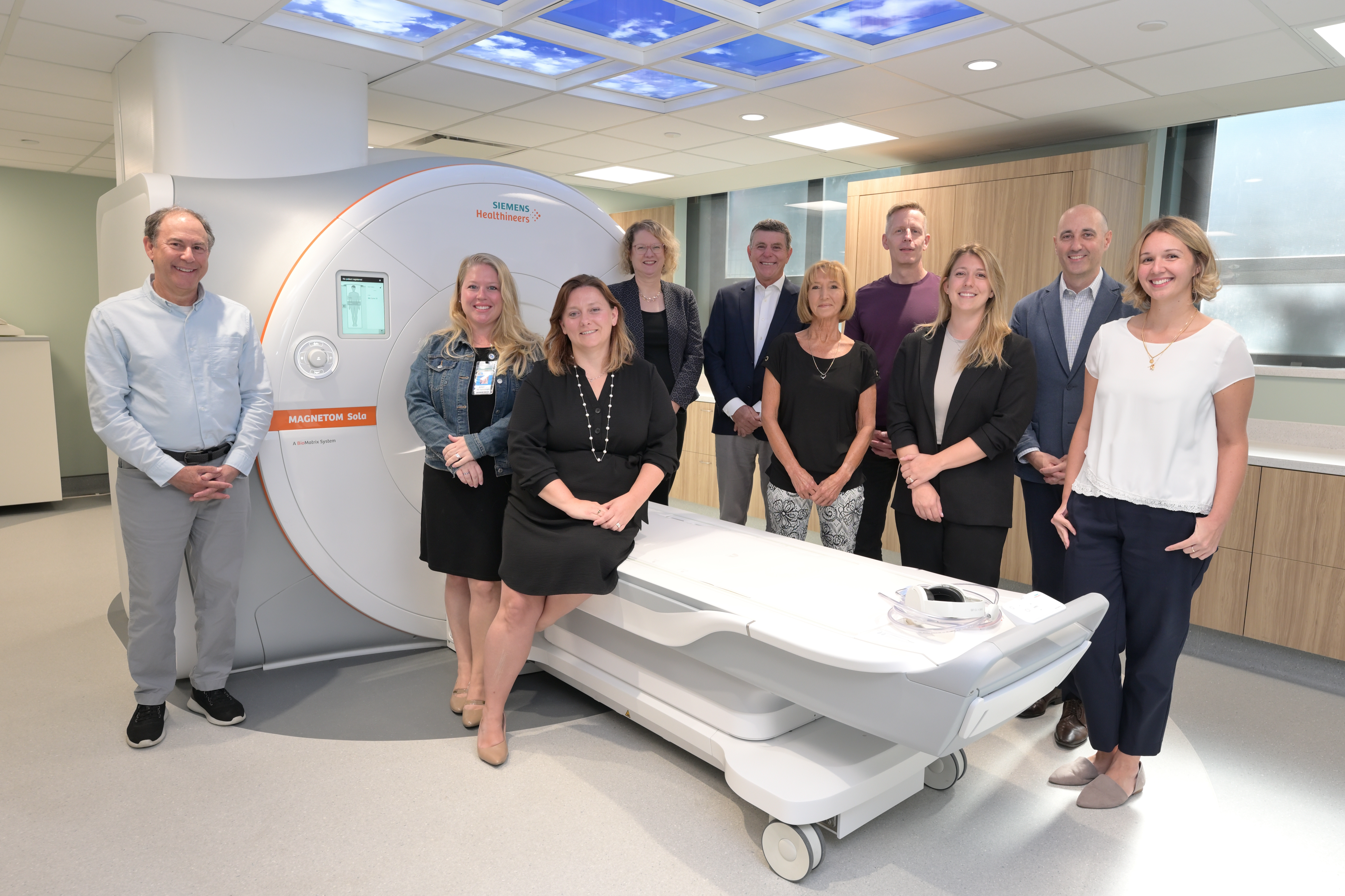 Group of men and women surrond an MRI machine in hospital MRI suite.